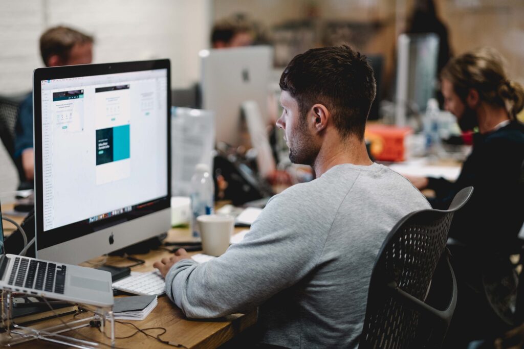 Man wearing grey sweater staring at computer screen while sitting at his desk